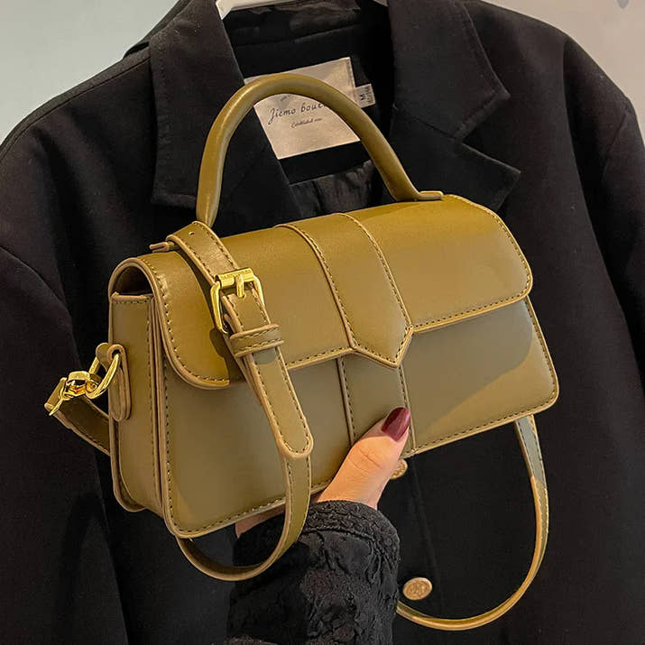 Stylish olive green women bag with adjustable strap and top handle on black coat background